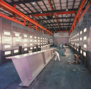 Worker painting a steel beam in the industrial coating area of a Greiner facility