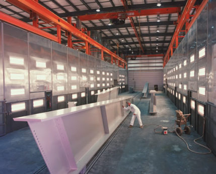 Worker painting a steel beam in the industrial coating area of a Greiner facility