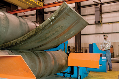 Worker operating Greiner's heavy plate roll machine to roll a steel plate at a Greiner facility