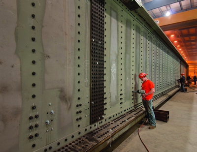 Worker drilling bolt holes in a fabricated railroad bridge at a Greiner facility